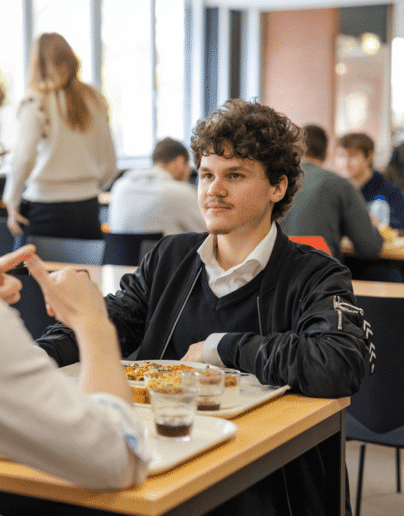 Un étudiant attentif discutant avec un camarade lors d'un déjeuner au restaurant universitaire de l'Université Catholique de Lille, illustrant la convivialité et les échanges entre étudiants sur le campus.