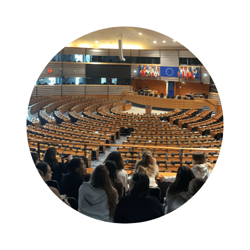 Vue d'un hémicycle parlementaire avec des étudiants assis au premier plan, face aux bureaux et aux drapeaux de l'Union européenne.