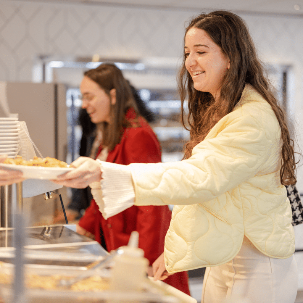 Une étudiante souriante se servant un repas au self-service d'un restaurant universitaire, accompagnée d'une autre étudiante.