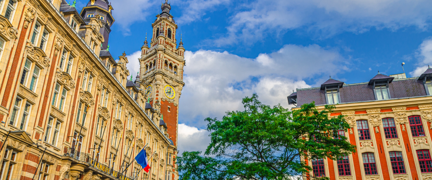 Vue en contre-plongée de la façade et du beffroi de l'Hôtel de Ville de Lille sous un ciel bleu nuageux.